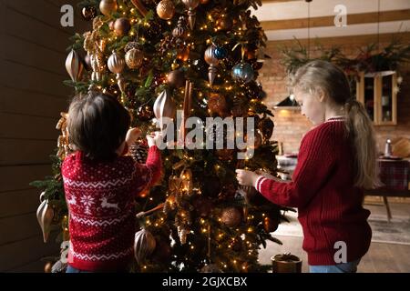 Happy little children siblings designing Christmas tree using decorative baubles. Stock Photo