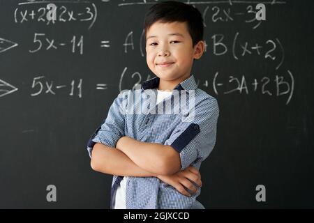 Portrait of happy proud asian boy standing on chalkboard background. Stock Photo