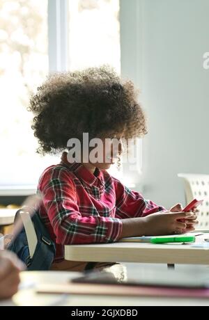 Happy smiling afro American schoolgirl using smartphone device in classroom. Stock Photo