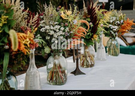 Rustic style. Boho style bouquets on the table in glass vases and jars. Wooden table and white tablecloth Stock Photo