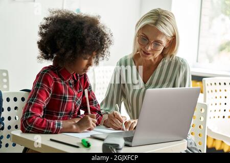 Afro American schoolgirl learning with female tutor teacher using laptop. Stock Photo
