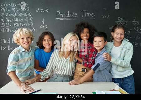 Portrait of cheerful smiling teacher and diverse schoolkids near chalkboard. Stock Photo