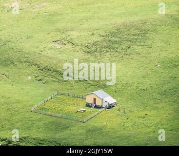 Aerial view with an empty sheepfold surrounded by fresh green pasture in Bucegi Mountains, Romania Stock Photo