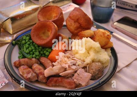 Plate full of Christmas dinner and Yorkshire puddings with cracker and mobile phone at side Stock Photo