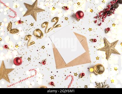 Open brown envelope with blank white card and numbers of 2022 for the coming year and festive seasonal decorations on white background. Top view. Stock Photo