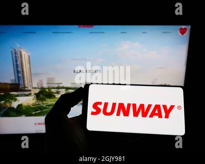Person holding cellphone with logo of Malaysian conglomerate Sunway Berhad on screen in front of business webpage. Focus on phone display. Stock Photo
