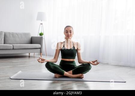 Calm serene european pretty millennial blonde lady practicing yoga, sitting in lotus position alone Stock Photo