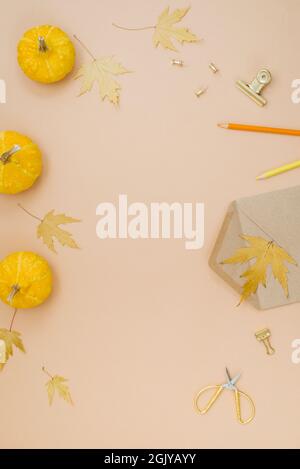 Autumn composition with small yellow pumpkins, fallen maple leaves, envelope, pen, pencils, clips and paper clips, and scissors on a beige background Stock Photo