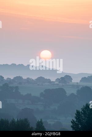 The low sun rises through hazy layers on a late summer morning in Lower Wharfedale, viewed from Farnely Park near Otley. Stock Photo