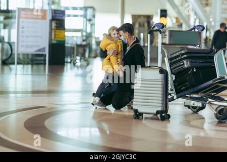 Woman with her son by sitting on knees at airport during pandemic. Mother and son waiting at airport during covid-19 outbreak. Stock Photo