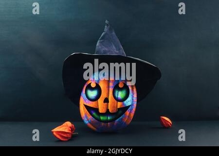 Halloween. A colourful pumpkin in black paper witch's hat and physalis on a dark background. Jack's lantern decorated by childrens. Copy space. Stock Photo