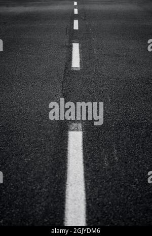 Dark gray asphalt road with white dashed line. High resolution full frame textured background in black and white. Copy space. Stock Photo