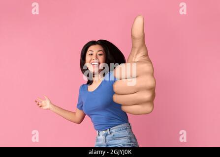 Emotional asian woman showing thumb up on pink Stock Photo