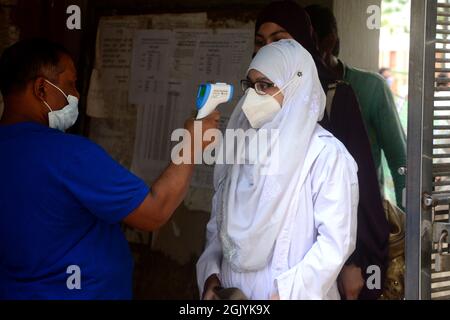 Dhaka, Bangladesh. September 12, 2021. An official checks the body temperature of a student upon her arrival at the Azimpur Government Girls School and College in Dhaka, Bangladesh, on September 12, 2021. After 543 days, primary, secondary and higher secondary schools across the country reopened maintaining Covid-19 guidelines and health protocols. Credit: Mamunur Rashid/Alamy Live News Stock Photo