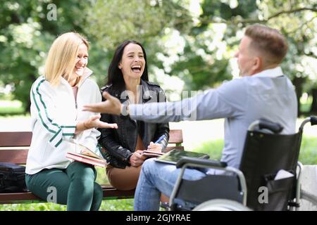 Disabled man in wheelchair communicating and laughing with women in park Stock Photo