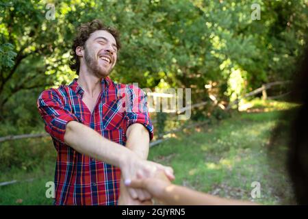 Happy boyfriend and girlfriend spinning together holding hands having fun under the trees outdoors in the park Stock Photo