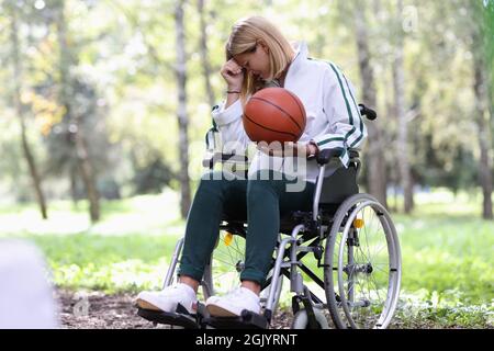 Disabled woman in wheelchair holding basketball ball and crying Stock Photo