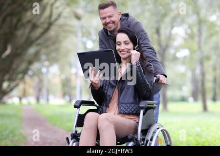 Disabled woman in wheelchair and man talking on digital tablet in park Stock Photo