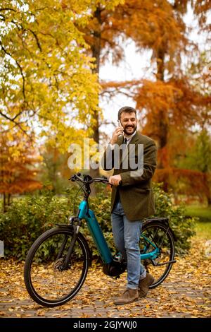 Handsome young man using mobile phone on electric bicycle at the autumn park Stock Photo