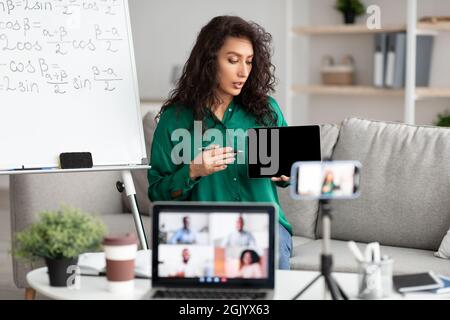 Female teacher explaining math online showing tablet to laptop Stock Photo