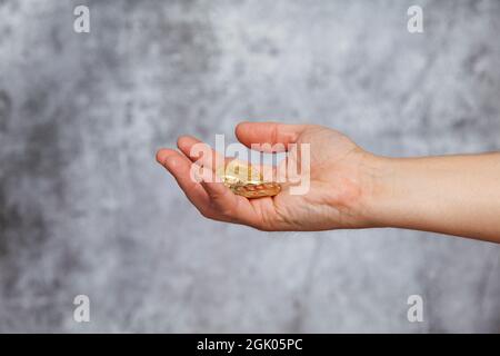 A man's right hand holding three golden Bitcoin coins on a textured gray background. Stock Photo