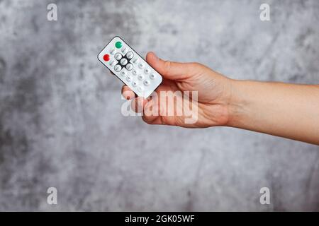 A man's right hand holding a small remote control of an electrical appliance on a textured gray background. Stock Photo