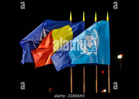 Otopeni, Romania - September 9, 2021: NATO, Romania, European Union and United Nations flags in the wind at night. Stock Photo