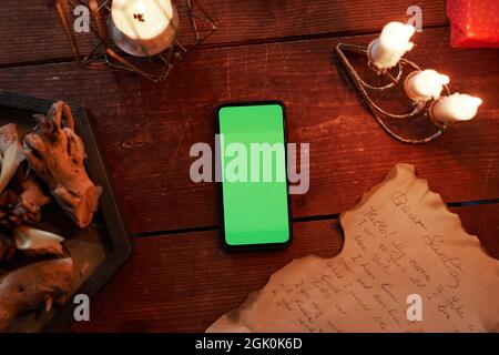Directly above view of smartphone with green screen, burning candles and letter on wooden table Stock Photo