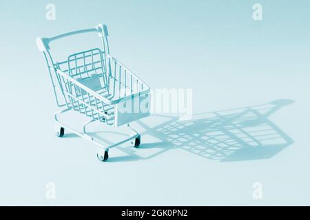 Empty mini blue shopping trolley with shadow on blue background. Minimalist style. Black Friday, season sale, discount concept. Stock Photo