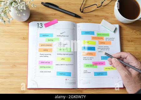 Hand of a woman writing appointments in a diary organizer or schedule calendar with a lot of colorful sticky notes for her time management on a wooden Stock Photo