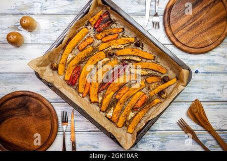 Place setting with wooden plates, rustic cutlery and baked pumpkin in baking tray on dining table. Healthy vegetarian food cooked for thanksgiving cel Stock Photo