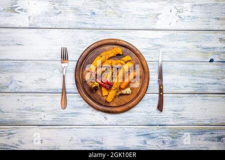 Roasted pumpkin slices and vegetable on wooden plate. Table top view of place setting with rustic cutlery. Tasty vegetarian dish. Copy space Stock Photo