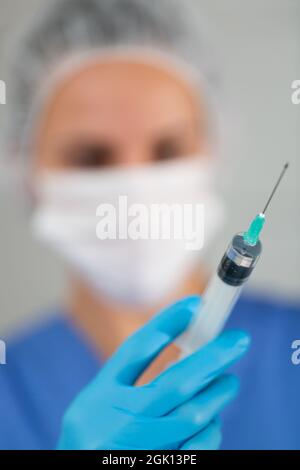 Masked female healthworker prepared a syringe for injection, filling it with medicine Stock Photo