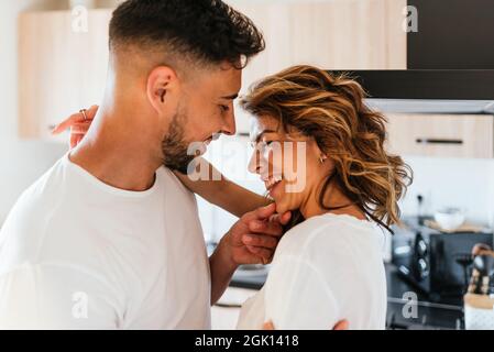 Lovely couple hugging and smiling while having fun together in the kitchen at home. Stock Photo