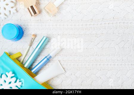 winter flat lay with cosmetics, makeup bag and snowflake on white knitted background. Stock Photo