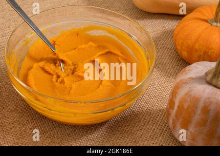 Pumpkin puree in a glass bowl, fresh pumpkin, squash, butternut close up on kitchen table Stock Photo