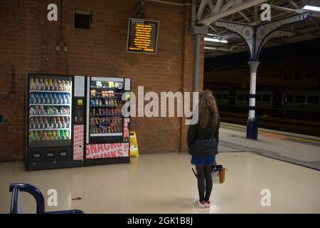 Doncaster, United Kingdom, 22nd May, 2021: Woman with long curly brunette hair and winter clothing contemplates which vending machine to purchase from Stock Photo