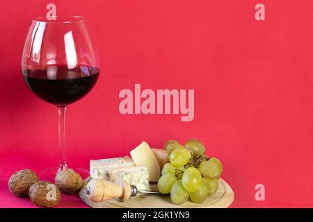 brie, gorgonzola, grapes, walnuts on a round wooden cutting board, a glass of red wine on a red background Stock Photo