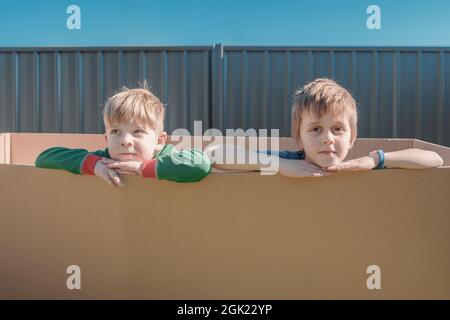 Little boys sitting inside a big carton box on the backyard Stock Photo