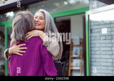 Senior Asian woman hugs friend meeting on modern city street Stock Photo