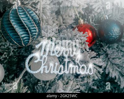Christmas background. Merry Christmas, celebration words with balls decoration on fir tree covered by white snow, close up. Stock Photo