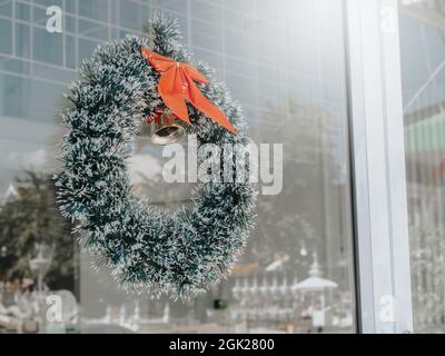 Christmas background. Christmas wreath ornate with red ribbon and a golden bell hanging on a clean glass door in front of the cafe. Stock Photo