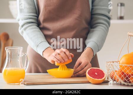 Woman squeezing grapefruit on table in kitchen Stock Photo