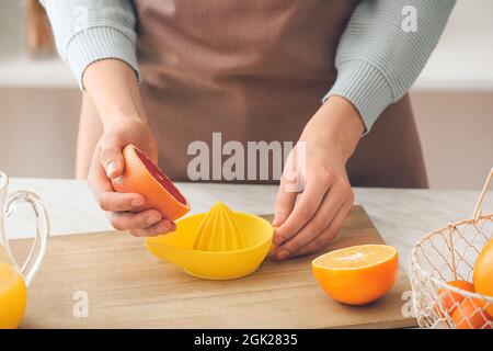 Woman squeezing grapefruit on table in kitchen Stock Photo