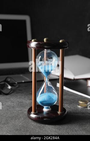 Stylish hourglass and laptop on dark table in office. Deadline concept Stock Photo