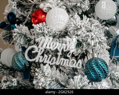 Christmas background. Merry Christmas, celebration words with balls decoration on fir tree covered by white snow, close up. Stock Photo