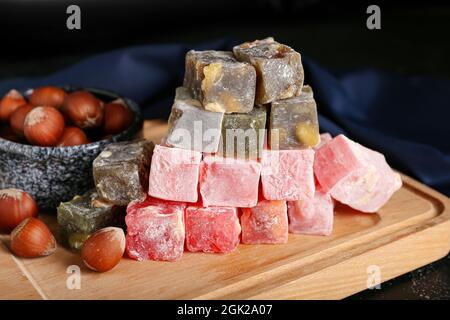 Wooden board with Turkish delight and hazelnuts on dark background Stock Photo