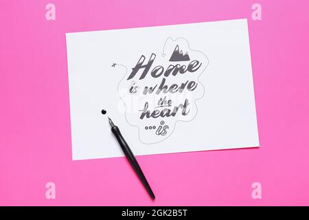 Paper with text HOME IS WHERE THE HEART IS and nib pen on pink background Stock Photo