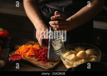 Young woman grating beetroot for delicious borscht on wooden board in kitchen Stock Photo