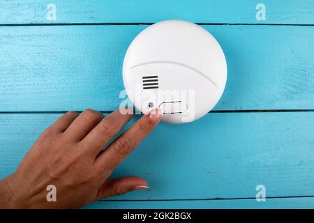 Smoke detector. Woman's finger presses the test button. Smoke, fire alarm. Stock Photo